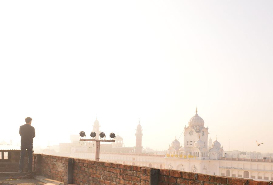 A figure on a rooftop facing the Golden Temple at dawn, Amritsar